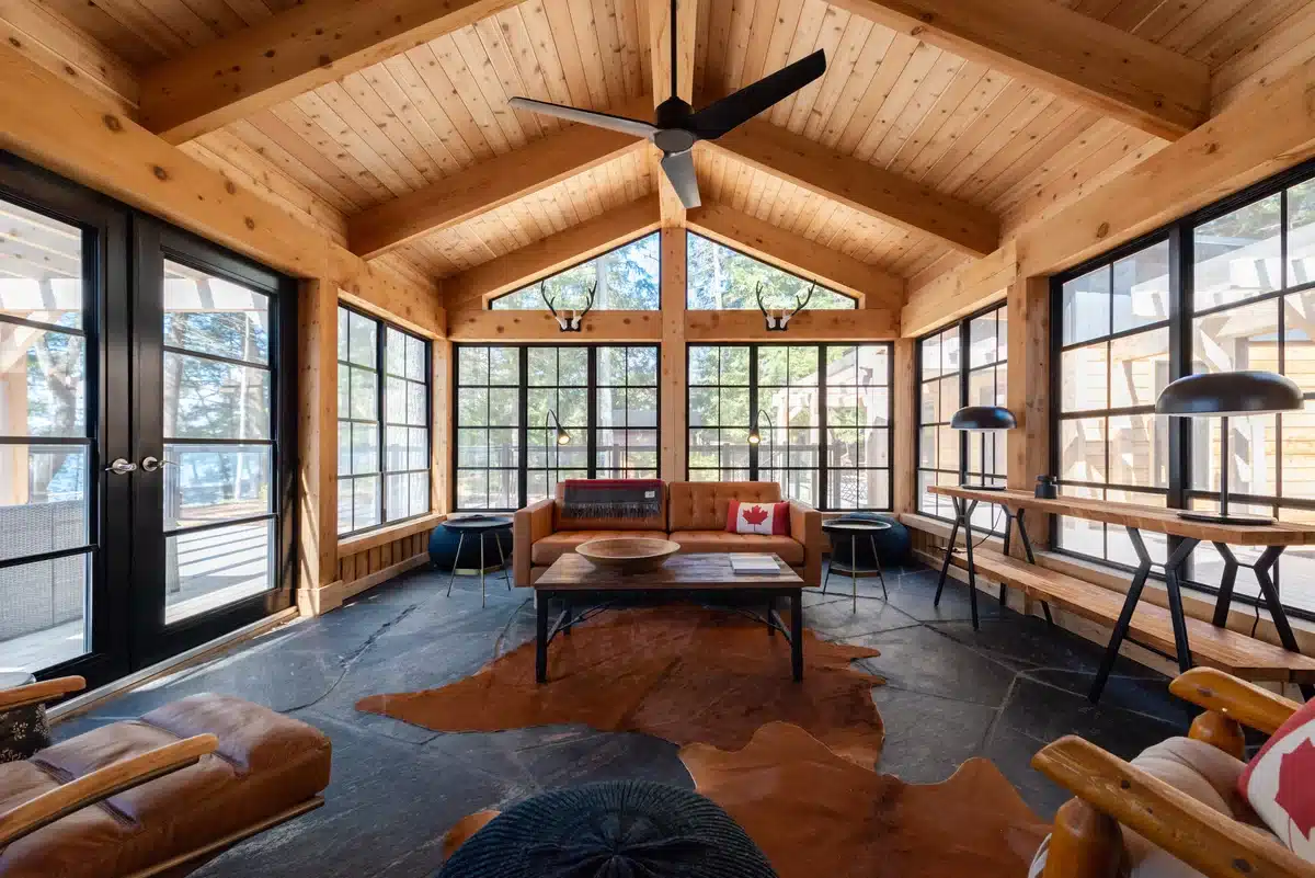 Interior views of rustic sunrooms featuring floor-to-ceiling WeatherMaster™ 4-track vinyl windows, timber-framed ceilings, and outdoor forest views.