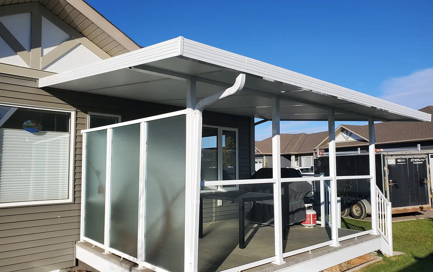 Side view of a white insulated patio cover installed on a residential deck, featuring integrated gutters and frosted glass privacy panels.